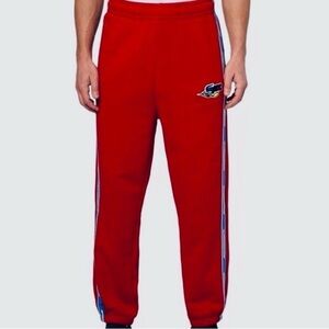 Lacoste NWT Men’s size medium red joggers with blue and yellow stripe accents.